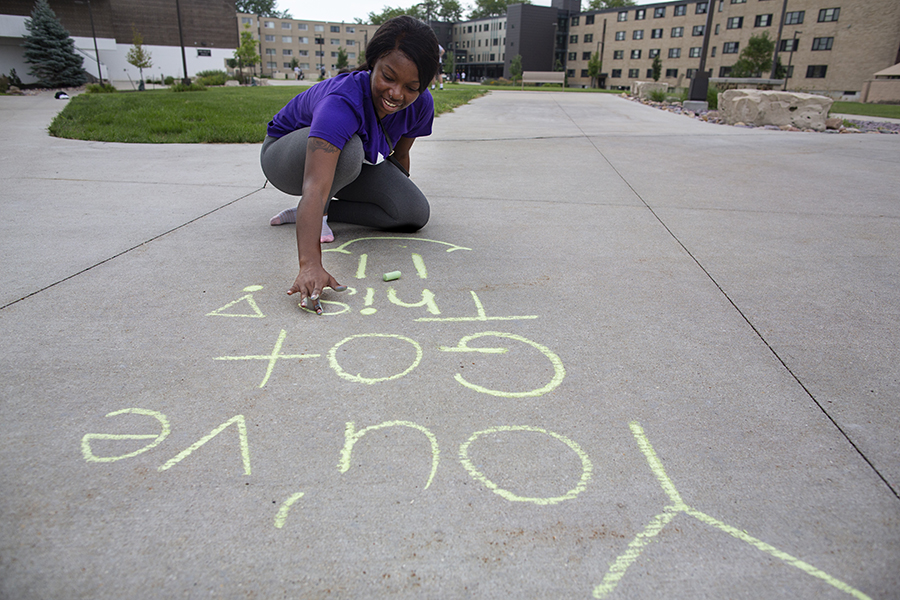 A student writes positive messages with chalk on a sidewalk.