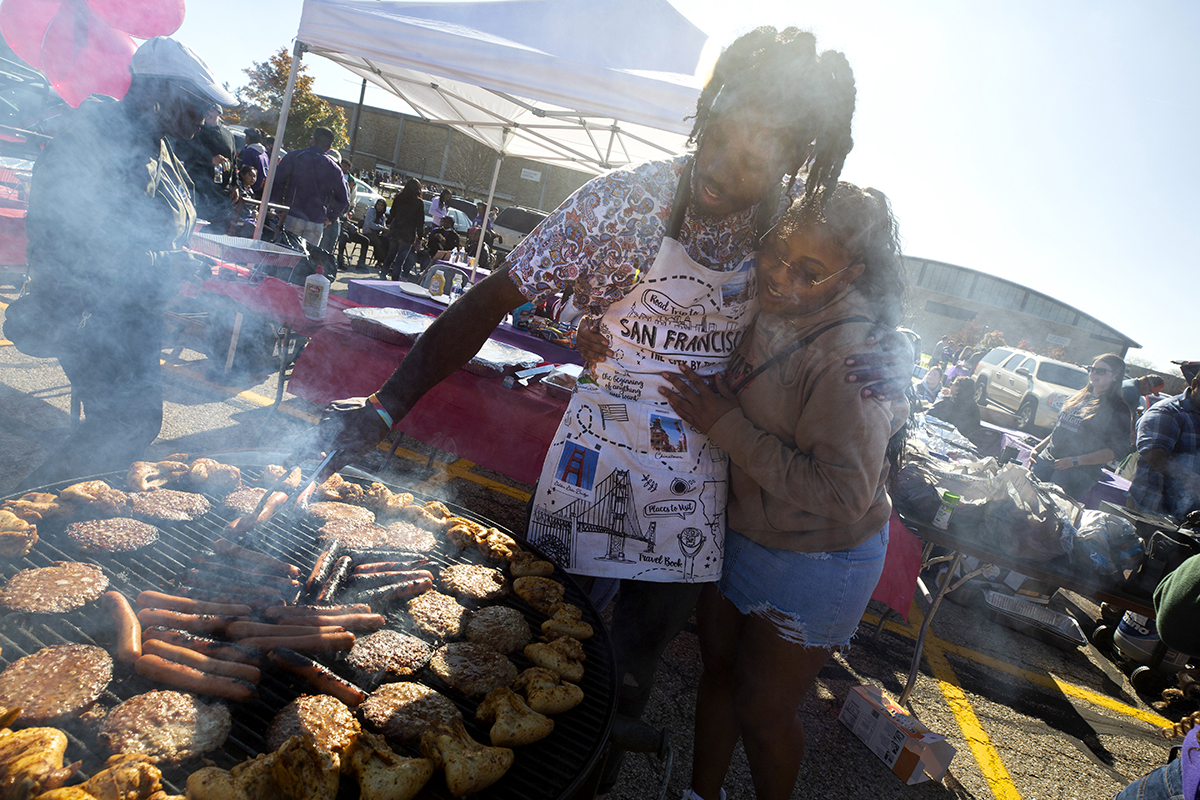 A picture of tailgating in the parking lot with lots of cars, pop-up tents and grills.