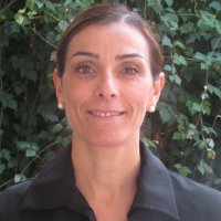 Ana Caballero Mengibar smiles while wearing a black shirt standing in front of green vines.