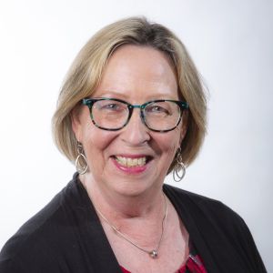 Janine Peterson smiles in front of a white wall while wearing a black shirt over a red shirt.