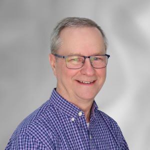 John Klinger smiles in front of a grey wall wearing a blue checked shirt.