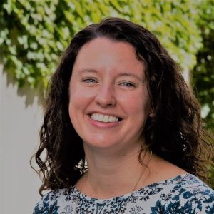 Lauren Burke wears a blue, flowery shirt while standing in front of a tree.