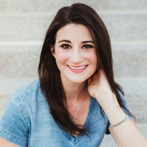 Gina Martin sits on a set of stone stairs wearing a blue shirt