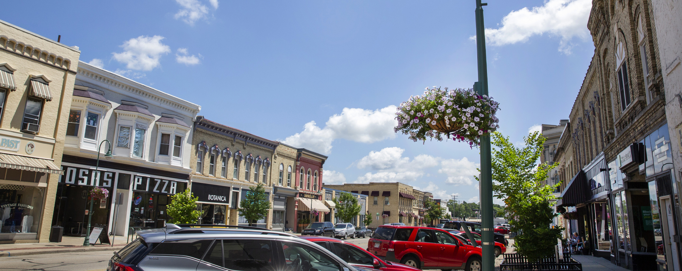 Buildings line the street in Downtown Whitewater with colorful flower pots hanging on the light posts.