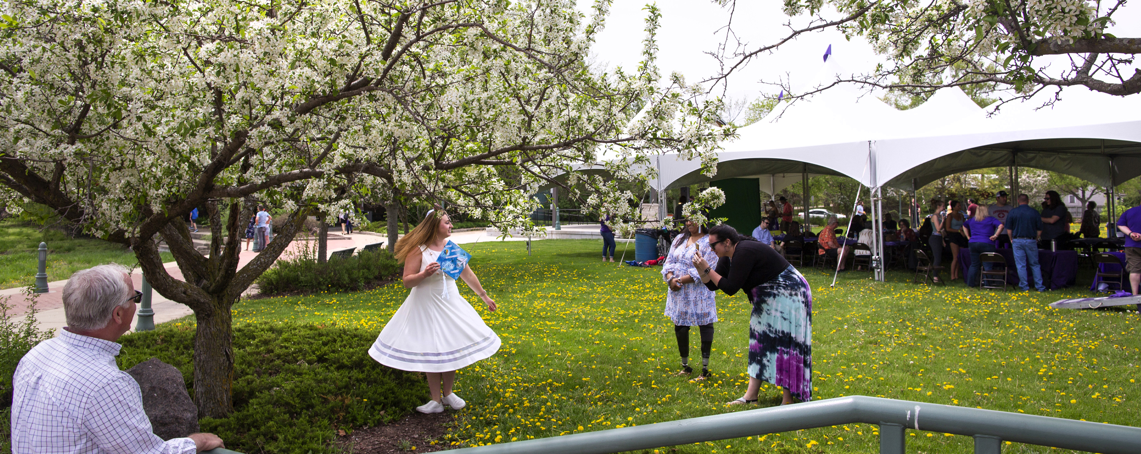 A person stands amongst flowering trees in a white dress and twirls as another person takes their photo.