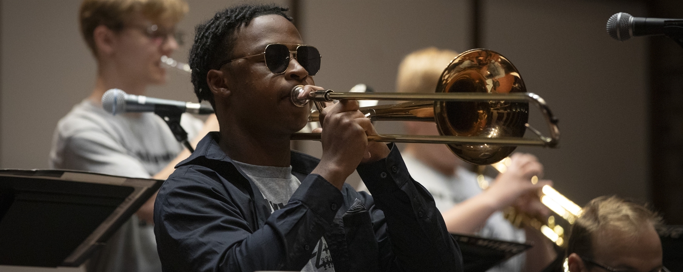 A trombone student performs during a lesson or rehearsal while another trombonist plays in the background, highlighting individualized brass instruction at UW–Whitewater.