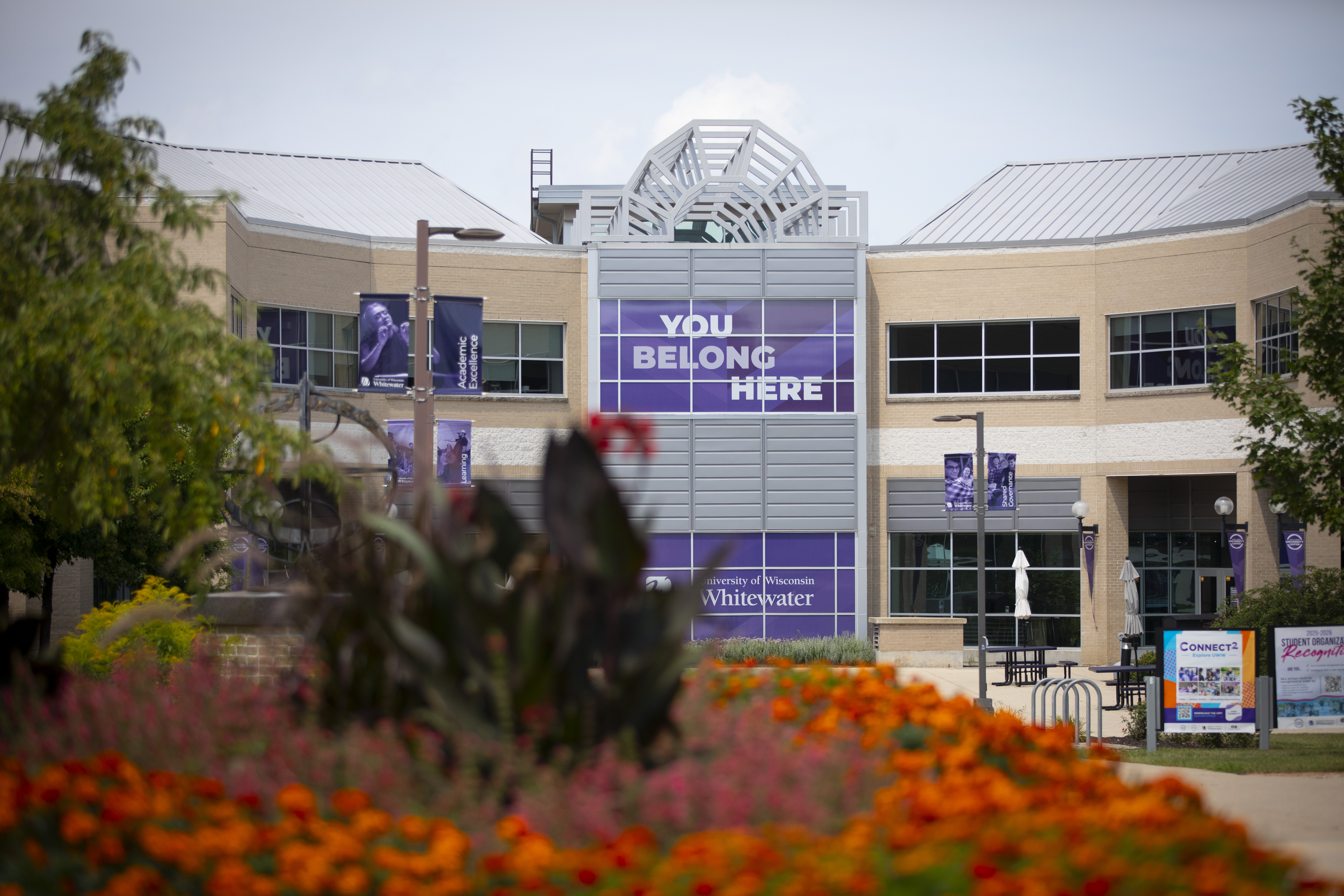 Flower bed with orange blooms in the foreground, the University Center in the background, and a statue displayed near the entrance on the UW–Whitewater campus.
