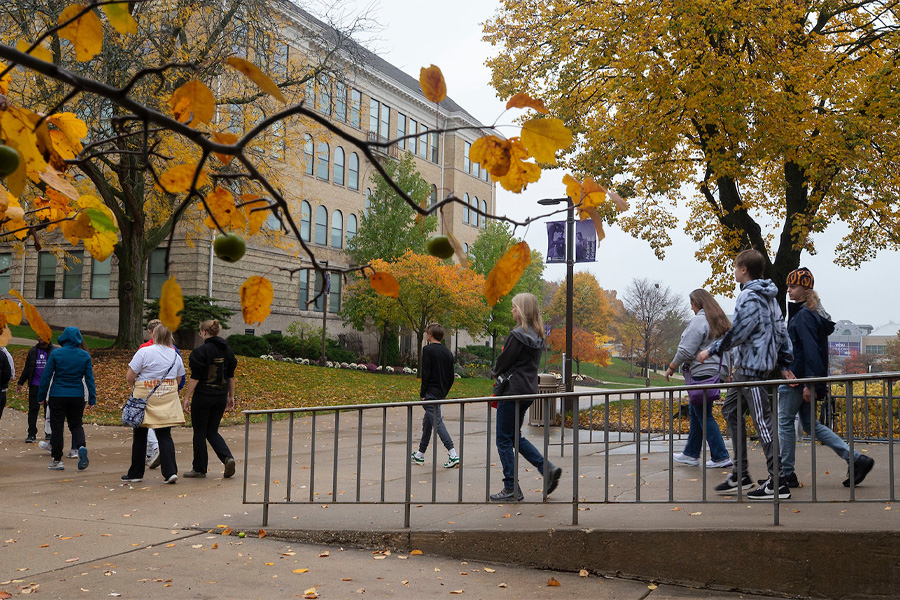 Students walk down a concrete ramp outdoors with colorful fall trees in the background.