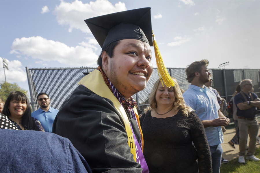 A student wearing graduate cap and gown smiles outdoors.