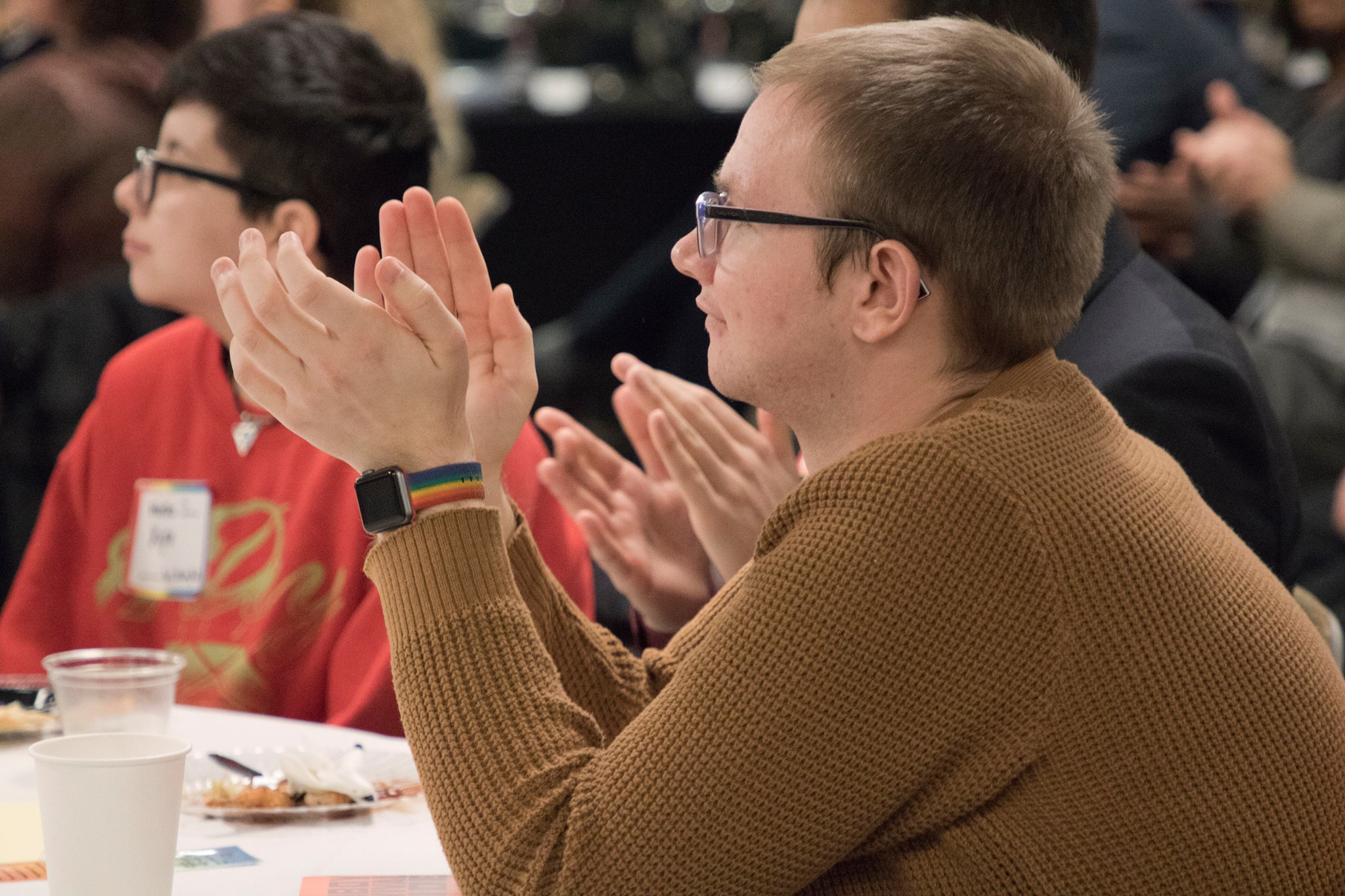 Two student sitting at a table watching a speaker. One is clapping. 