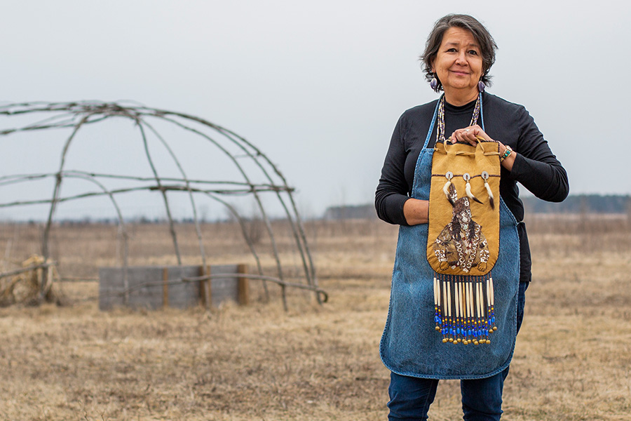 A photo of Artist Melanie Tallmadge Sainz standing outside holding Native art.