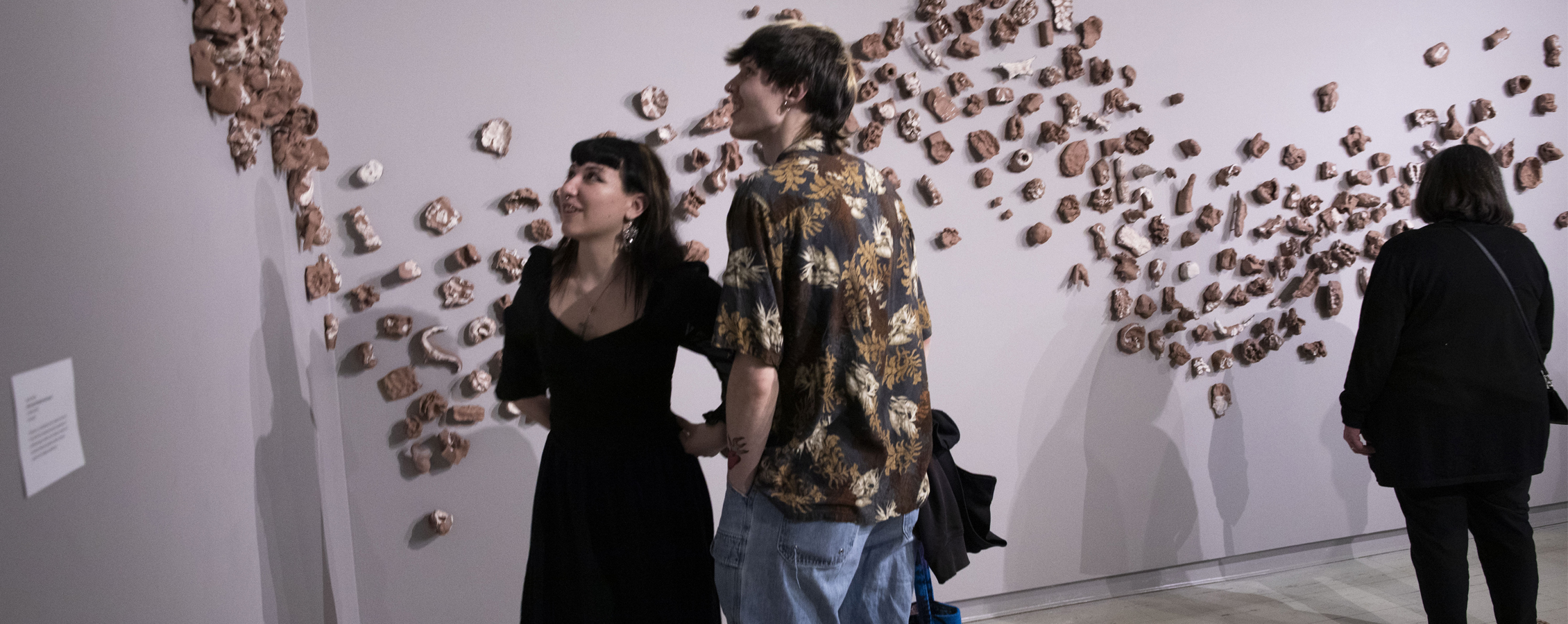 A group of people gather in the Crossman Gallery with one person speaking at the front of the gallery.