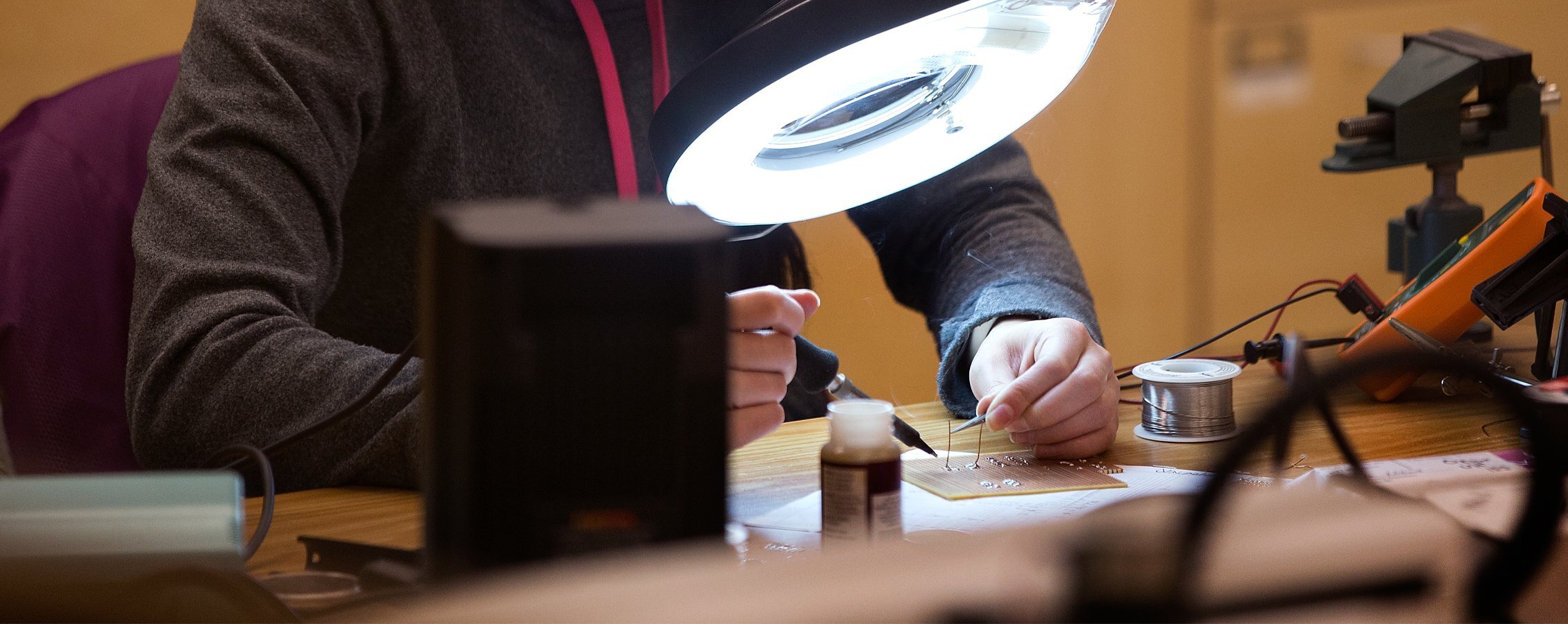 A student solders groups of micro wires under a large light.