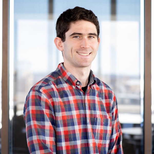 Photo of Caleb Flack sitting in front of a window wearing a red and blue plaid shirt