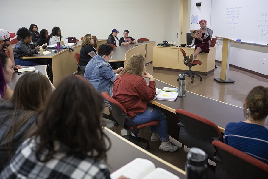 Jacob Tobias, a guest speaker, reads from a book at the front of a class.