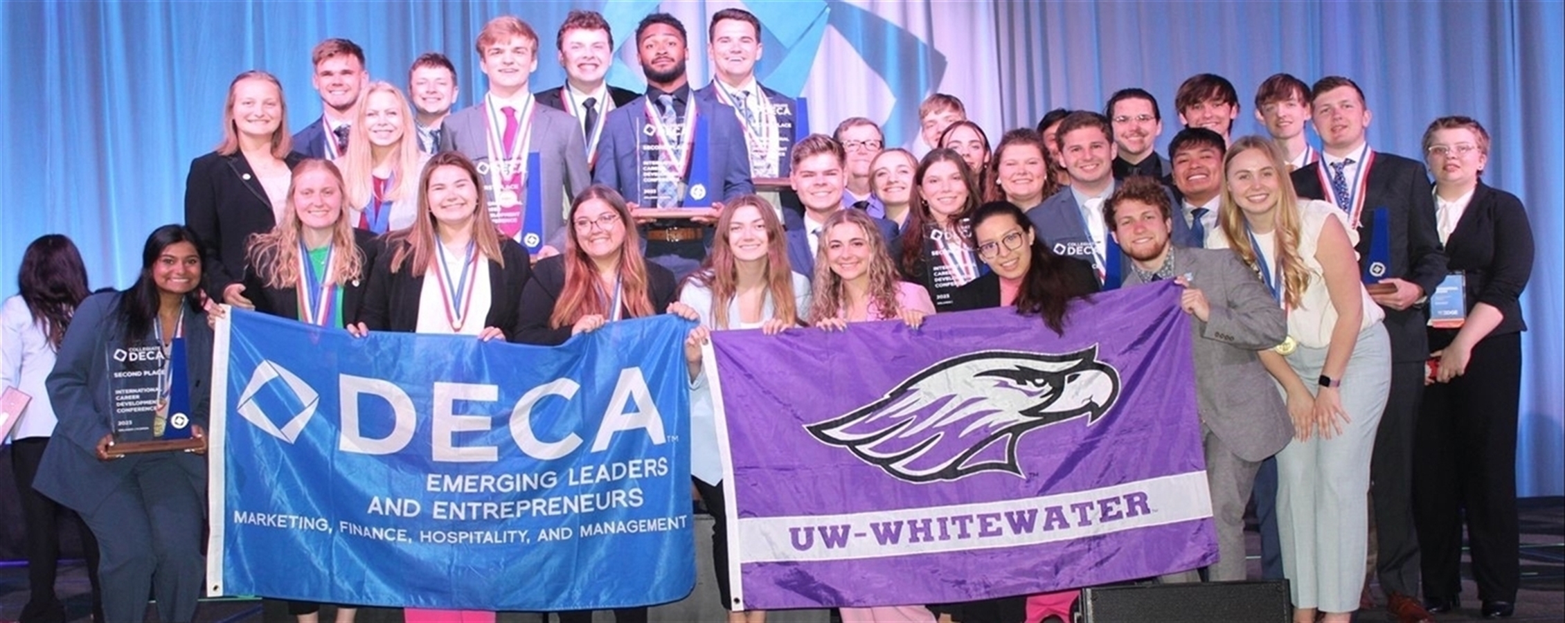 DECA students posing with awards and UW-Whitewater flag and DECA flag