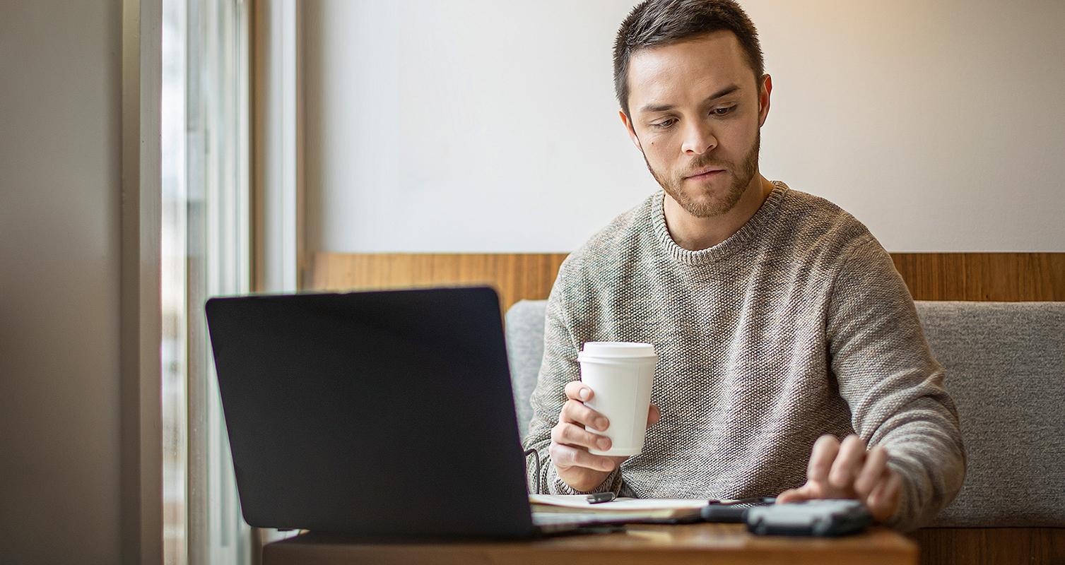 Man studying in cafe with laptop and textbook