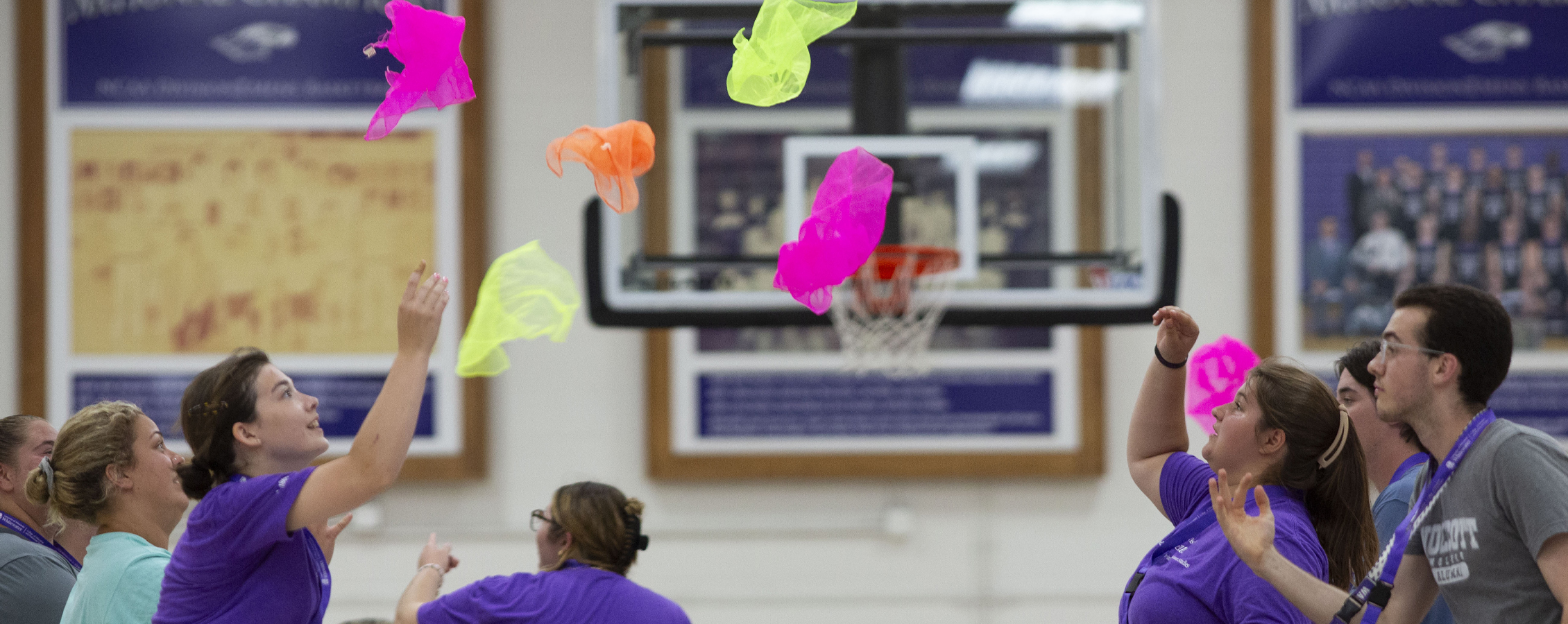 Students in purple shirts toss colorful handkerchiefs into the air.