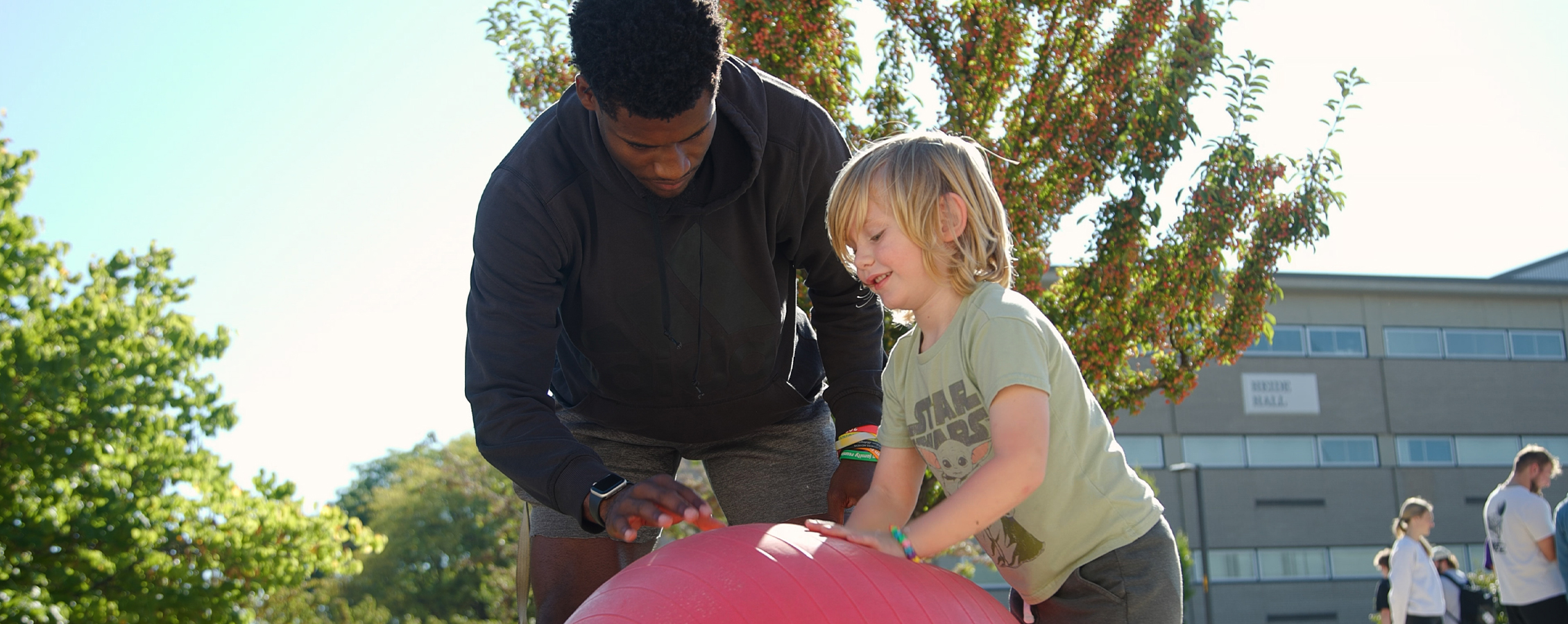 A student shows a child how to bounce a large red ball.