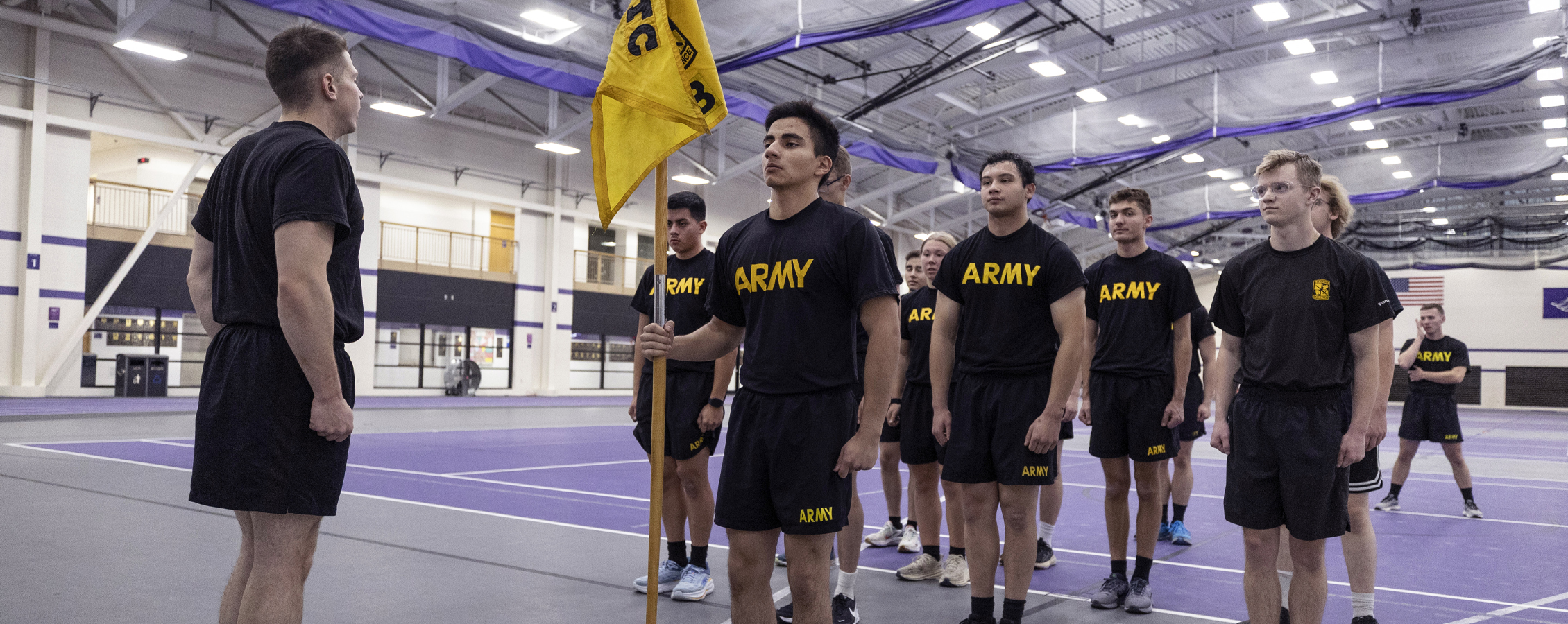 People wearing black shirts that say Army line up military-style in the fieldhouse.