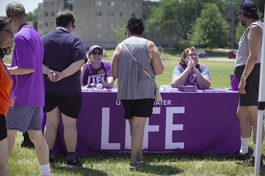 People visit an outdoor table with a purple banner that says LIFE program.