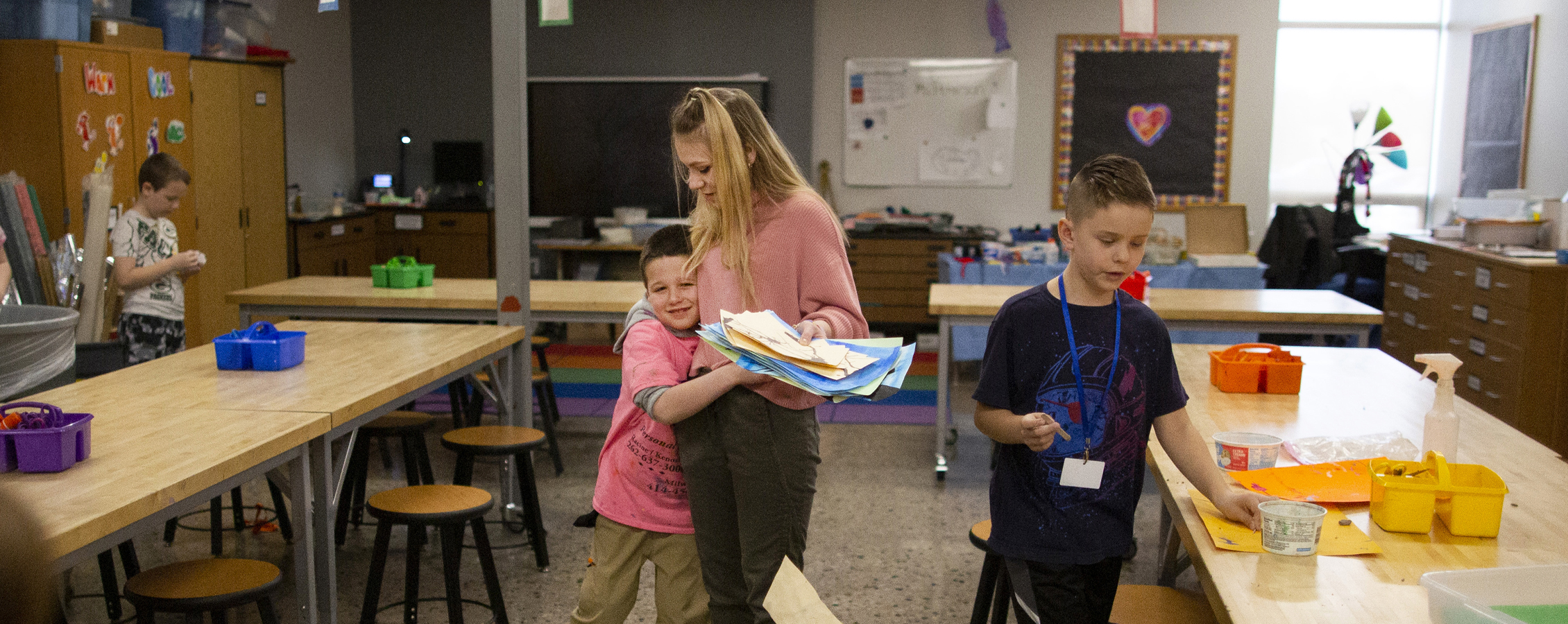 A student teacher sits amongst high schoolers and performs a demonstration on paper.