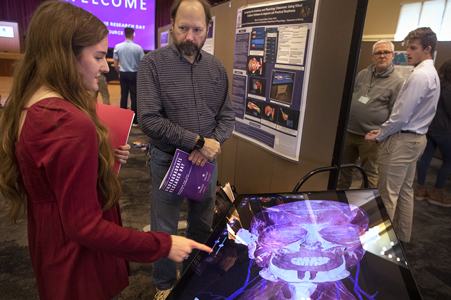 A student shows work to a faculty member on a virtual image of the muscular system of a human head and neck.