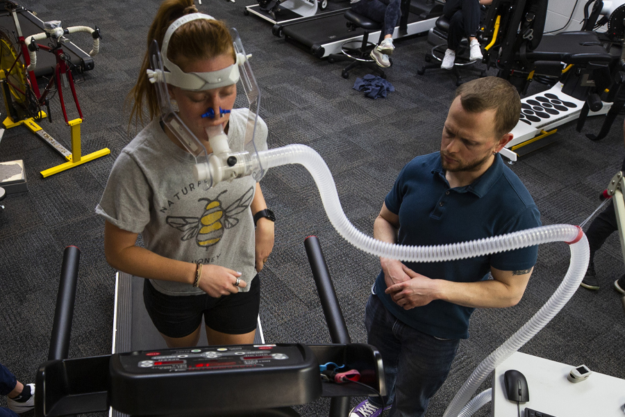 A student runs on the treadmill with a tube connecting from her face to a computer.