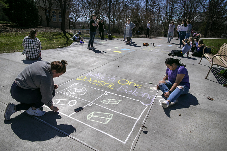 Students write math problems on a sidewalk with challk.