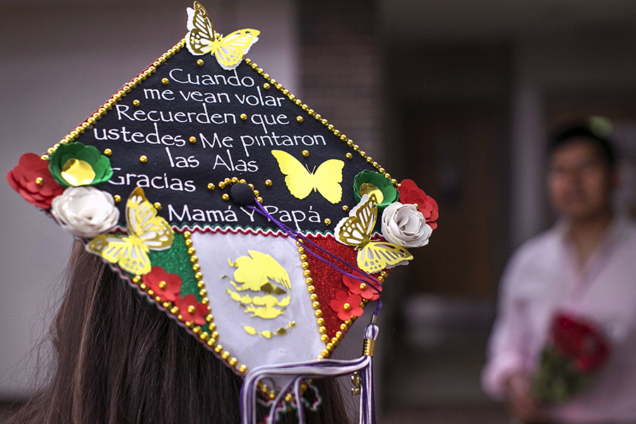 A student's cap at graduation is colorfully decorated with butterflies, a Mexican flag and Spanish language.