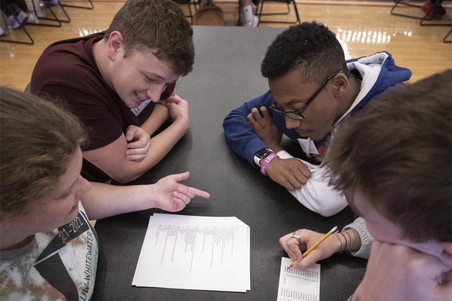 A group of students sit together at a table and look at a piece of paper with notes on it.