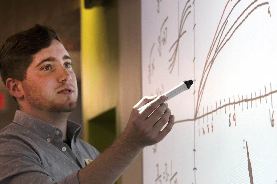 A person stands at a white board with a marker in their hand and draws a mathematical graph.