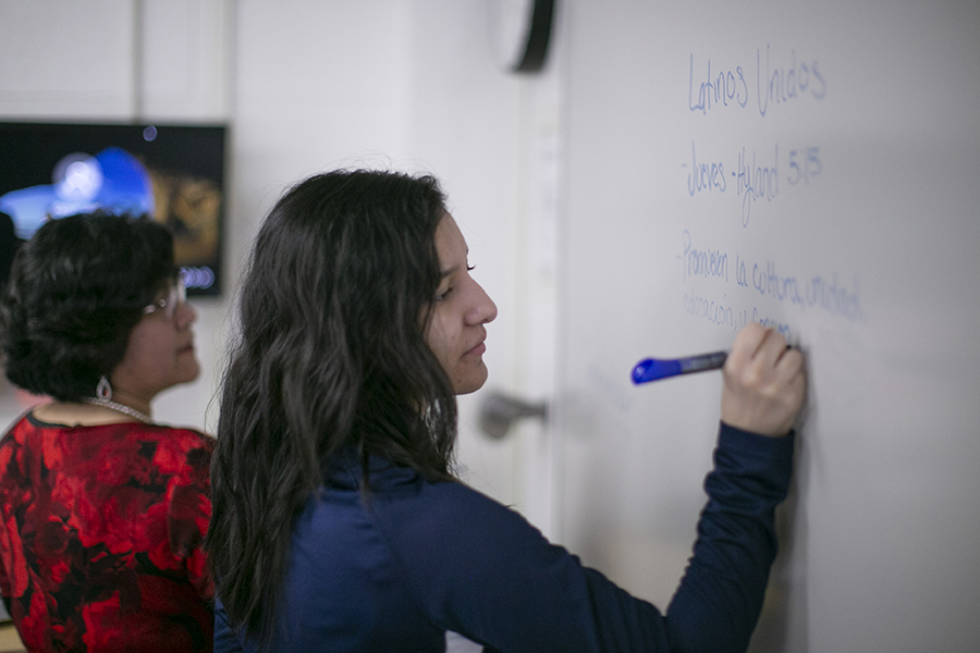 A student writes in Spanish on a whiteboard as a faculty member looks on.