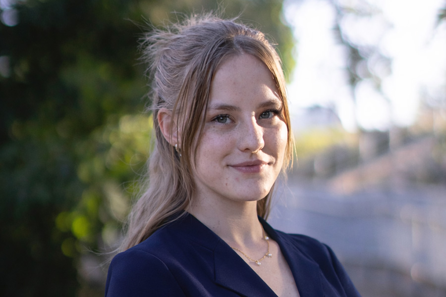 Brianna Kaptur stands outside in front of trees with a walking path in the background.