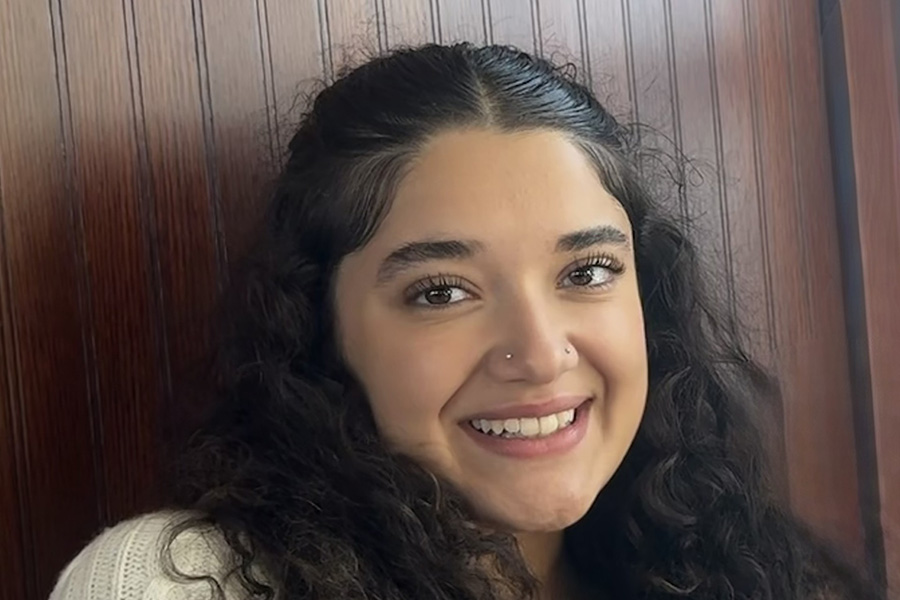 Favi Sanches smiles while leaning against a wooden wall.