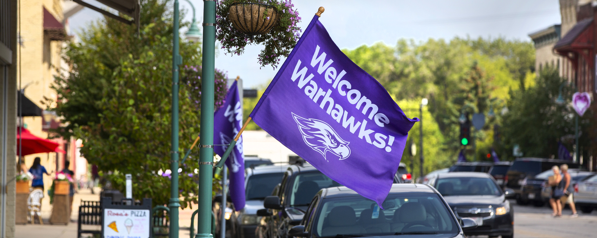 A purple flag that says welcome Warhawks hangs off a business in downtown Whitewater.