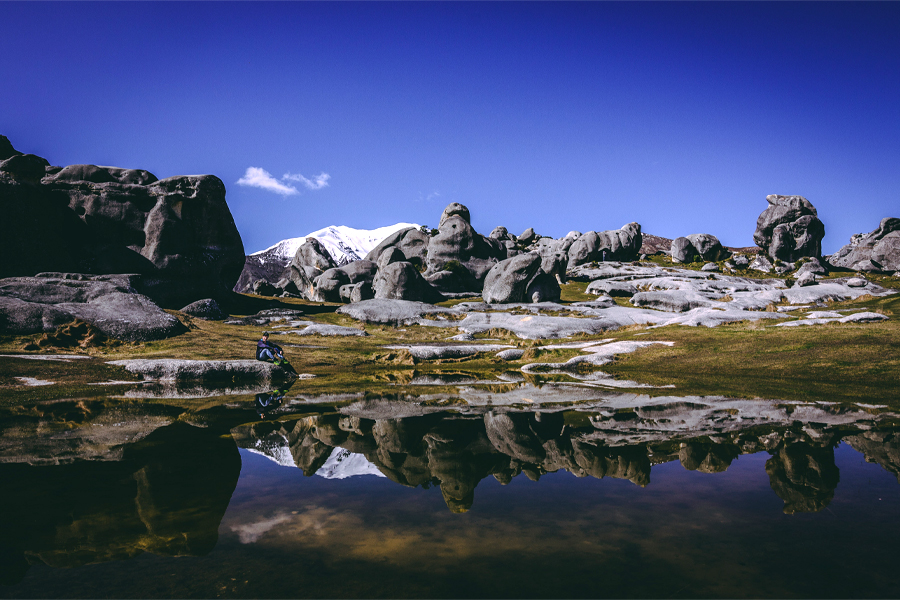 A person sits next to a pool of water amidst trees and mountains.