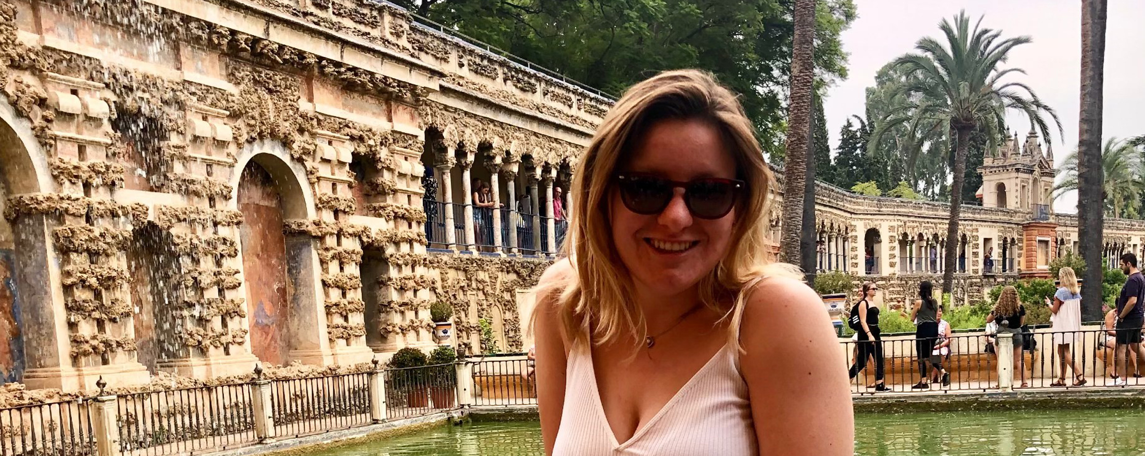 A young adult who is standing amidst a mediterranean style building smiles at the camera.