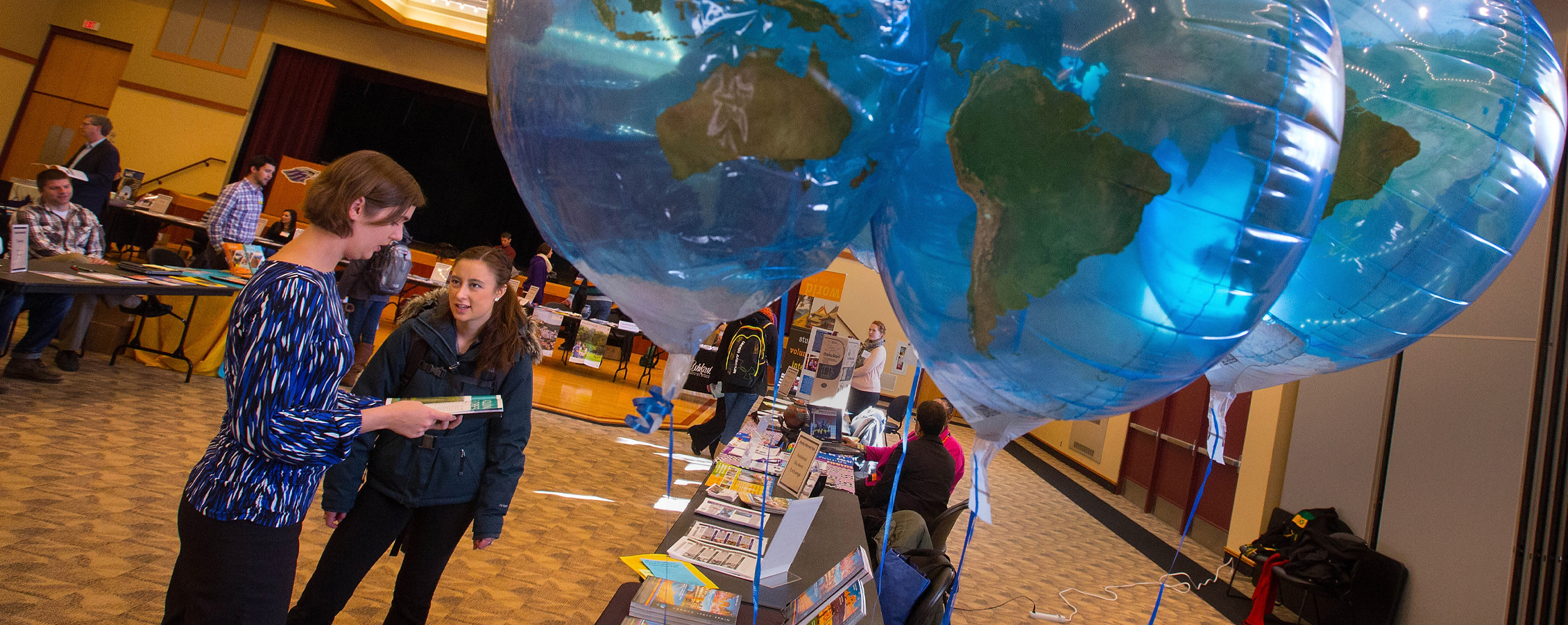 Two people talk in the Hamilton Room of the University Center with blue balloons in the foreground.