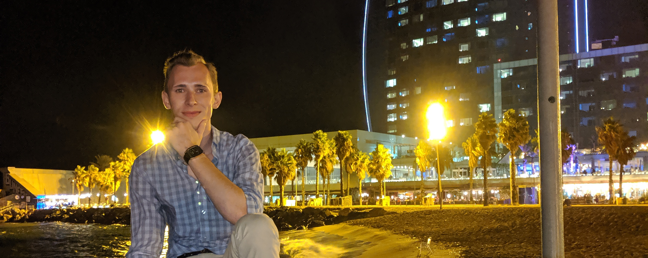 A person smiles at the camera with city lights behind them.