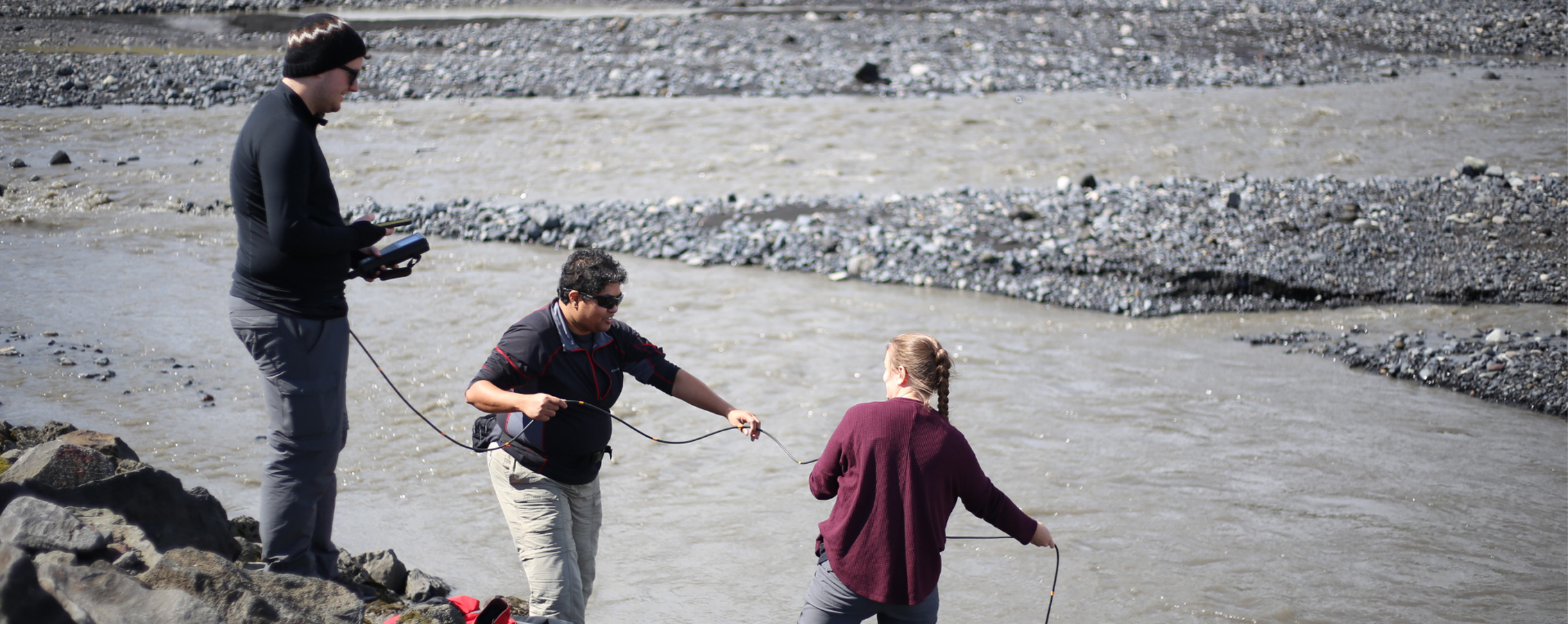 Three people work together and use technology to test a body of water.