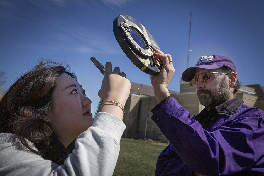 International student Bona Jeon photographs the sun through a solar filter held by an associate professor of physics.