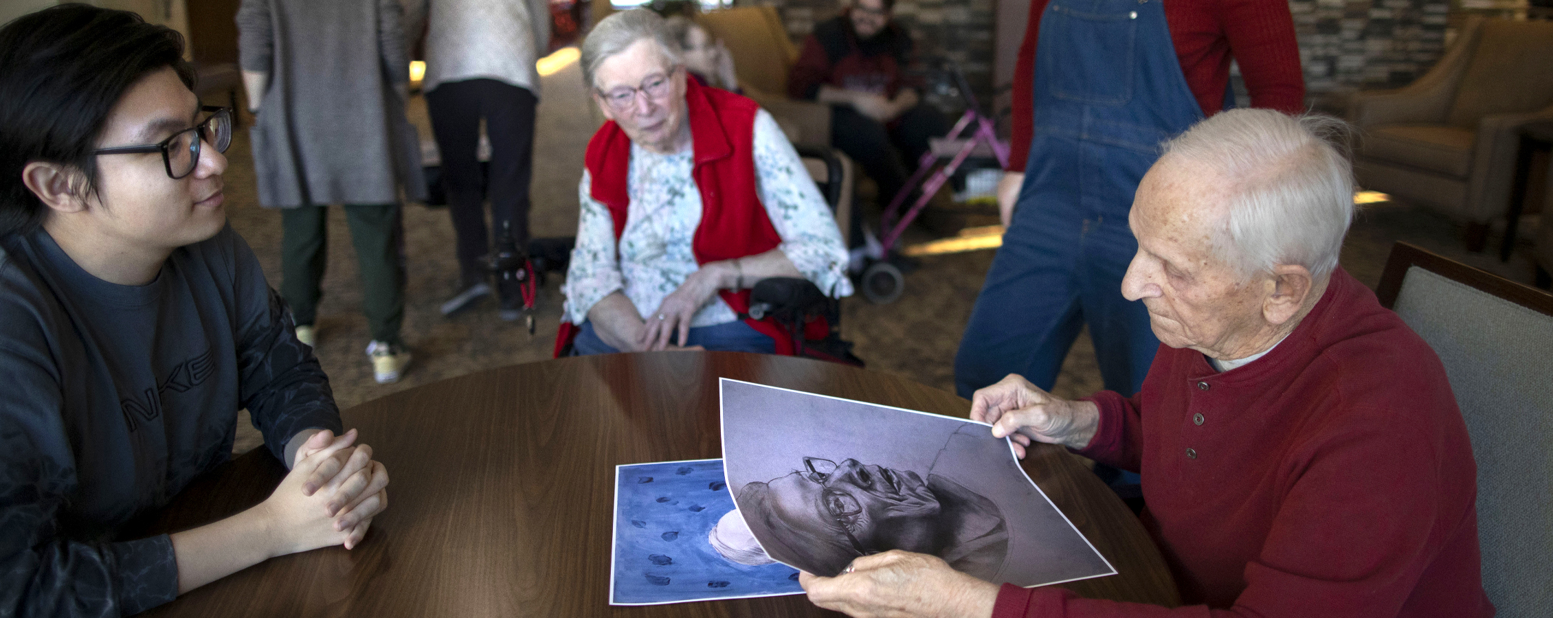 An international student hands a person a hand drawn portrait.