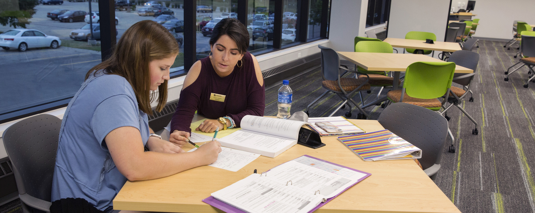 An international student from Venezuela tutors another student at a table.