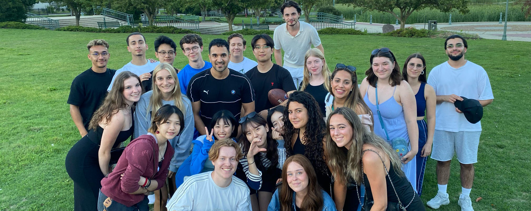 A group of international students celebrate with a red, white, and blue cake in a park.