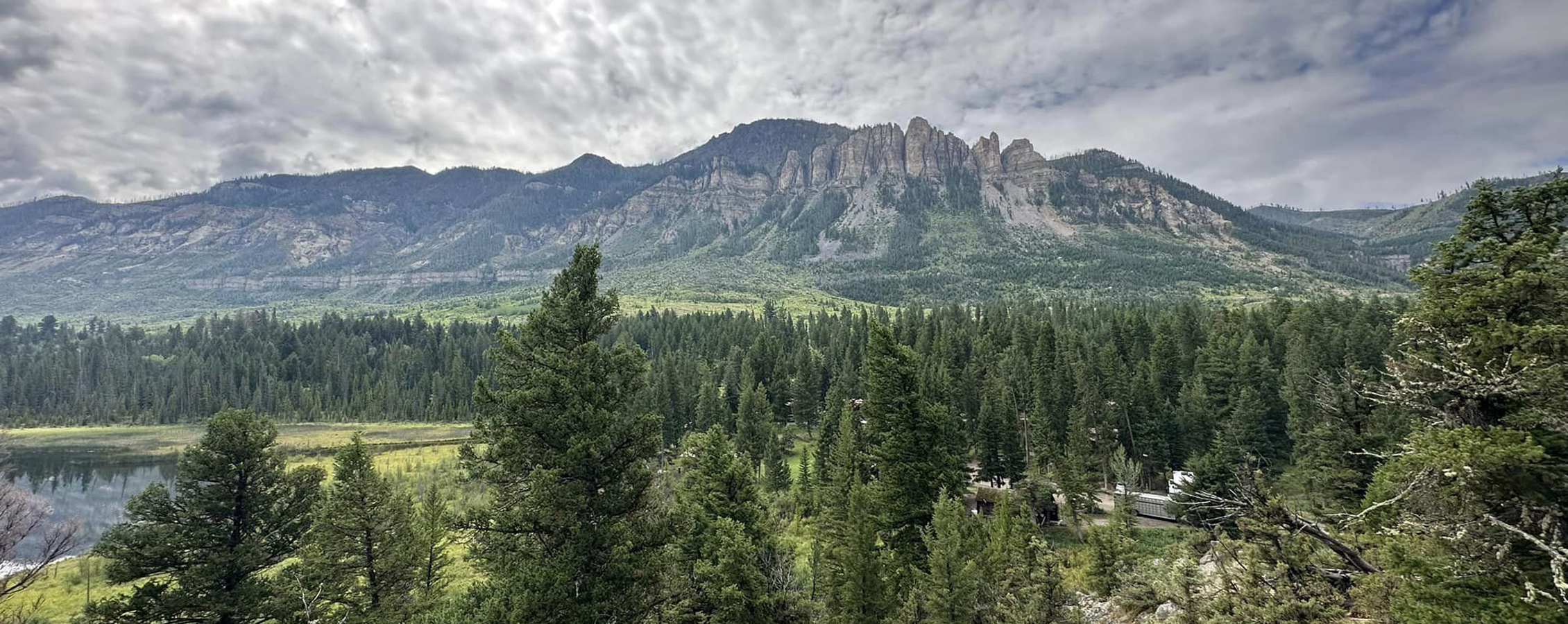 Landscape photo of clouds over a mountain with a forest in the foreground.