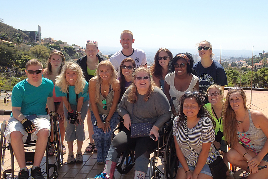 A group of people smile at the camera with mountains and clouds behind them.