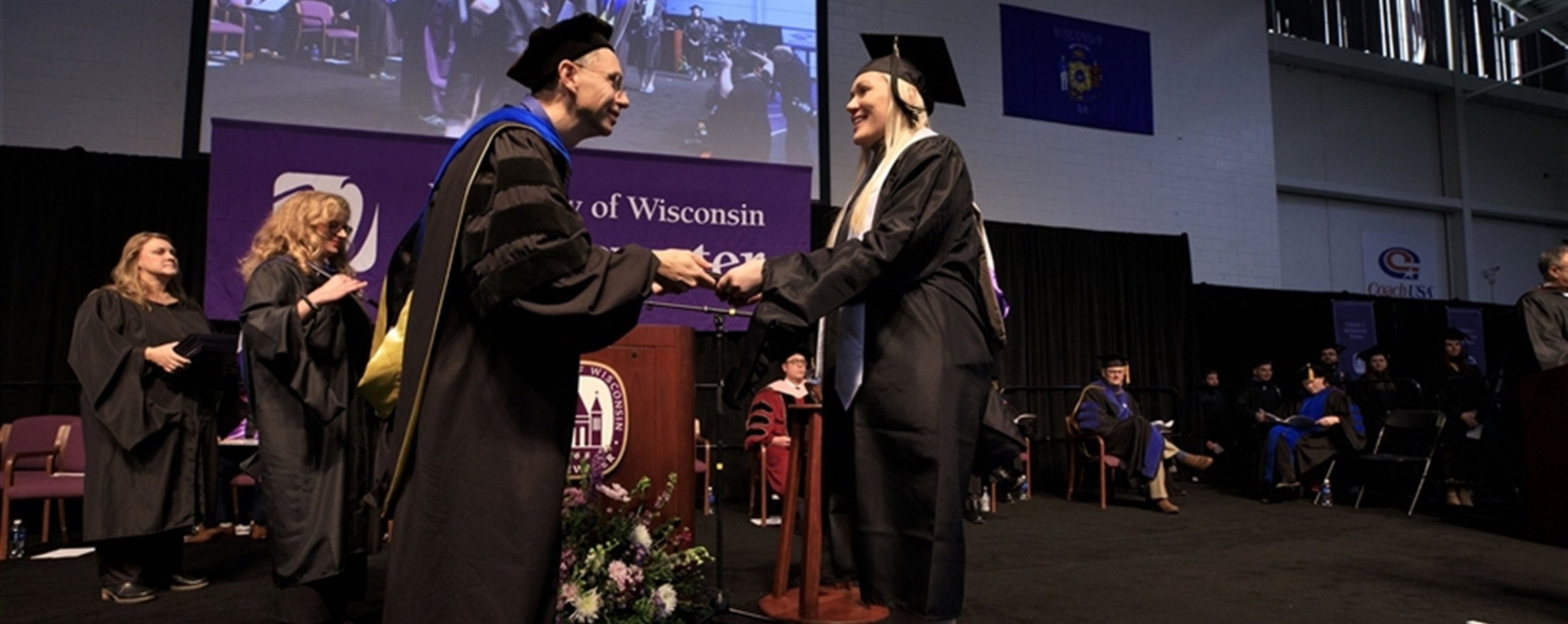 Dean Vick shakes Veena's hand as she crosses the graduation stage at UW-Whitewater