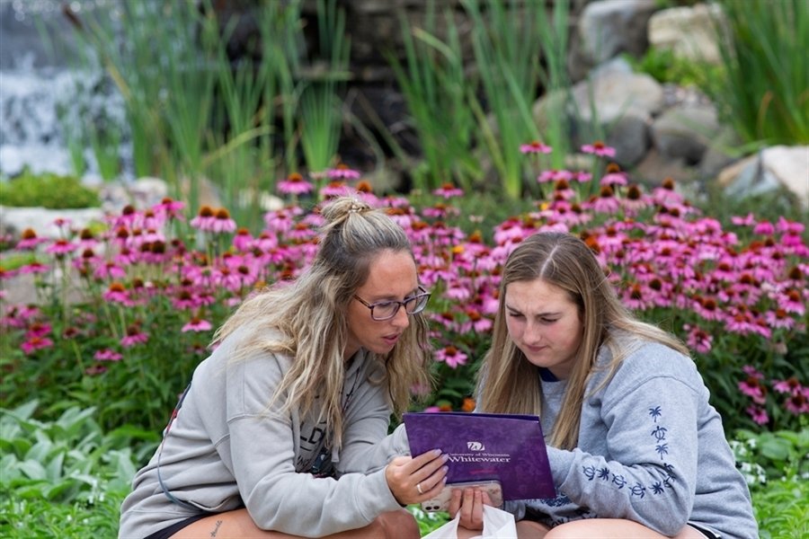 Students reading a handout in front of flowers on campus.