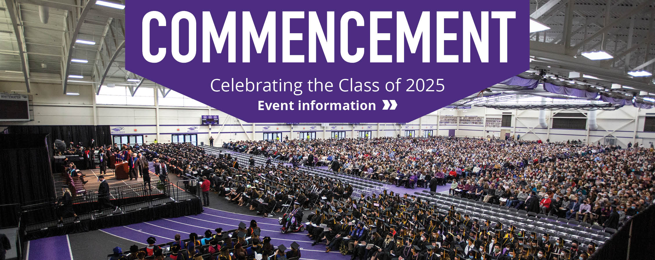 People fill the fieldhouse during a commencement ceremony with the words Commencement across the top.